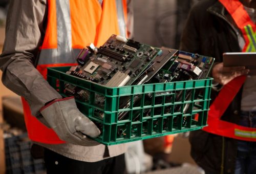 Portrait of female and male recycling coworkers holding digital tablet and plastic box full of old mother boards while looking at the camera