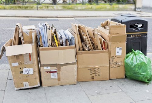 A neatly arranged stack of discarded cardboard boxes awaiting collection by refuse disposal crew on a street pavement in London.